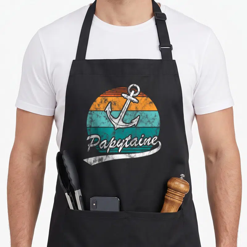 Tablier de cuisine noir avec ancre blanche vintage sur disque orange et turquoise et texte Papytaine en script blanc.