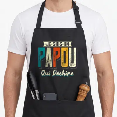 Tablier de cuisine noir avec l'inscription Je suis un papou qui déchire en typographie colorée et décontractée.