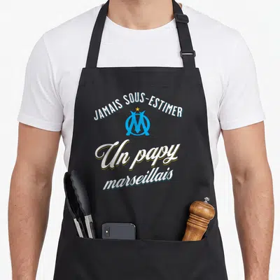 Tablier de cuisine noir avec logo OM bleu et texte blanc Jamais sous-estimer un papy marseillais