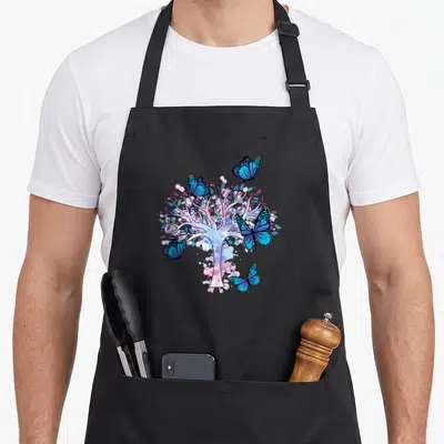 Tablier de cuisine noir avec un arbre de vie blanc entouré de papillons bleus et de touches de rose aquarelle.