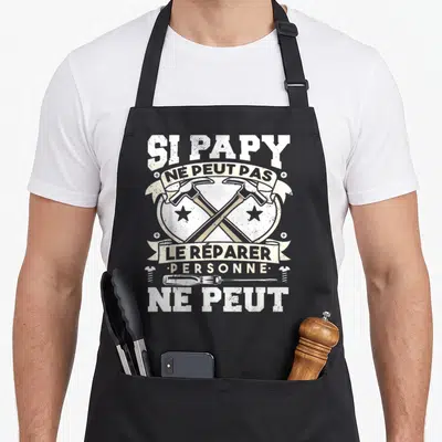 Tablier de cuisine noir avec deux marteaux croisés et une vis imprimés en blanc et beige sur le devant.