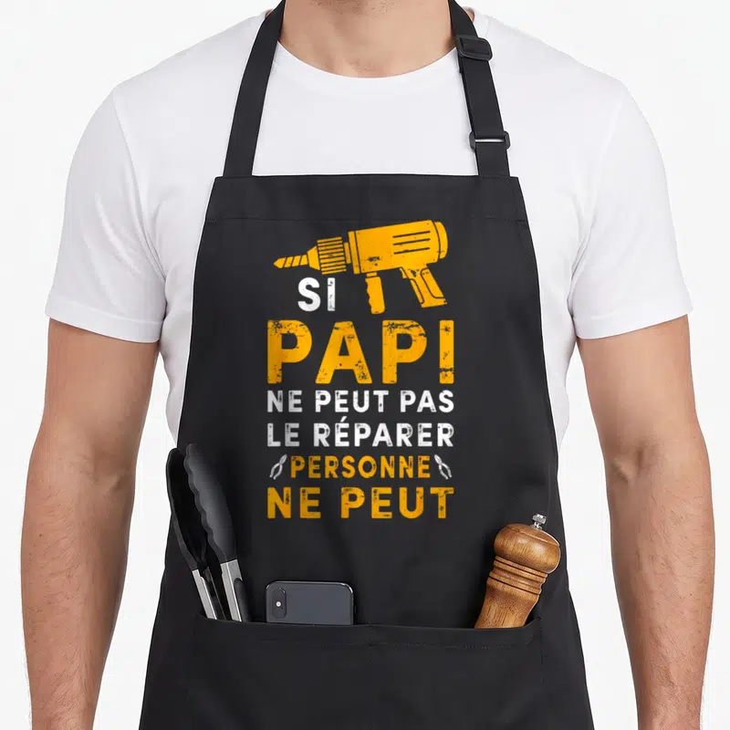 Tablier de cuisine noir avec une perceuse orange et le texte Si Papi ne peut pas le réparer personne ne peut en blanc et orange.