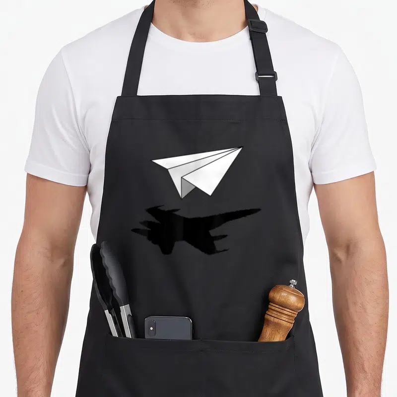 Tablier de cuisine noir avec un avion en papier blanc projetant une silhouette de chasseur stealth noir.