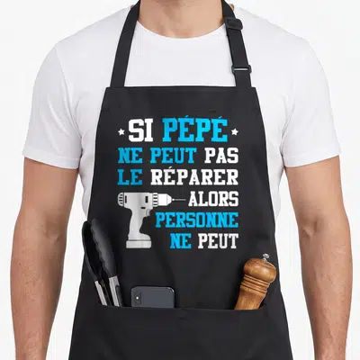 Tablier de cuisine noir avec inscription blanche et bleue et illustration de perceuse électrique blanche au centre du motif.