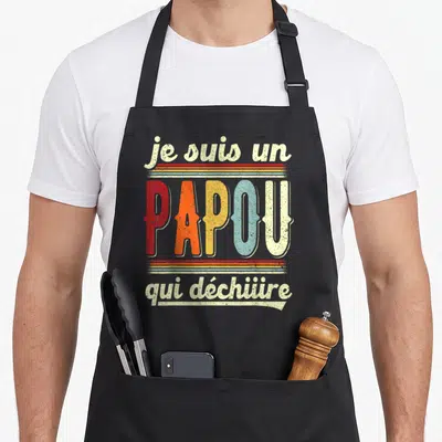 Tablier de cuisine noir avec inscription rétro « je suis un papou qui déchire » en lettres colorées.