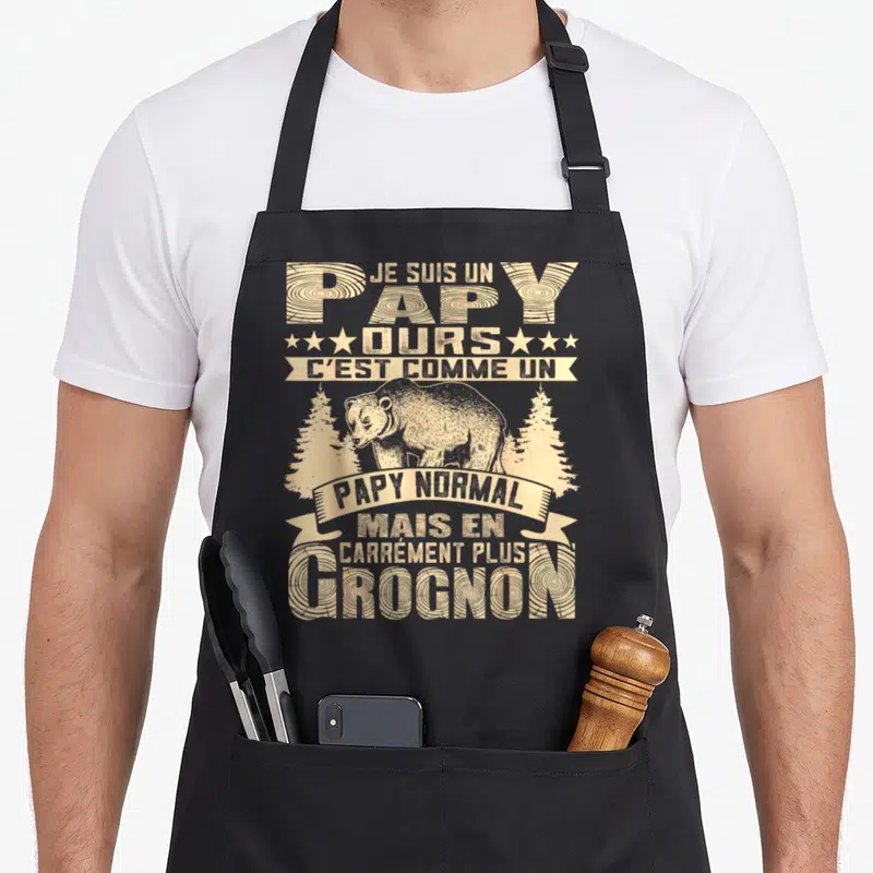 Tablier de cuisine noir avec illustration d'ours et texte beige sur fond gris uni