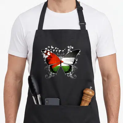 Tablier de cuisine noir avec un grand papillon aux couleurs du drapeau palestinien entouré de motifs floraux blancs stylisés.