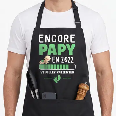 Tablier de cuisine noir avec inscription Encore Papy en 2022, illustration d'un bébé et icône de chargement verte.