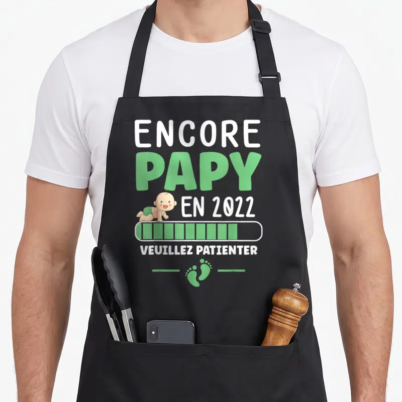 Tablier de cuisine noir avec inscription Encore Papy en 2022, illustration d'un bébé et icône de chargement verte.