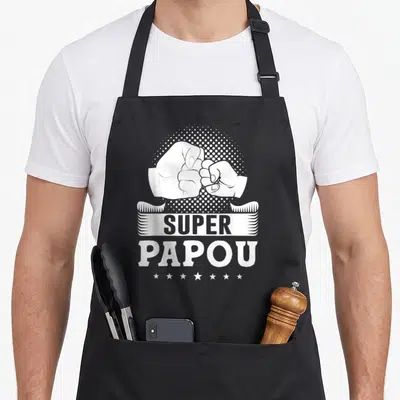Tablier de cuisine noir avec illustration blanche d'un poing de serré et linscription Super Papou surbande ornée d'étoiles.