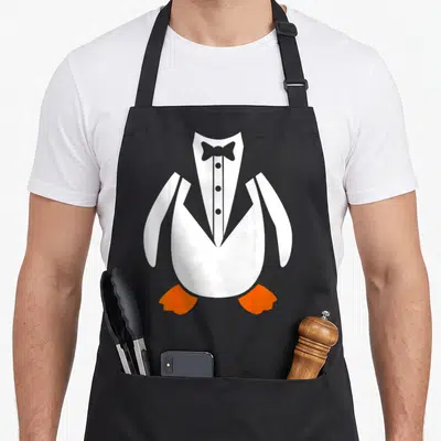Tablier de cuisine noir avec illustration d'un pingouin vêtu d'un costume frac blanc et d'un noeud papillon gris.