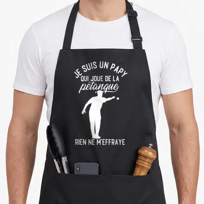 Tablier de cuisine noir avec une silhouette blanche d'un homme jouant à la pétanque et du texte humoristique en blanc.