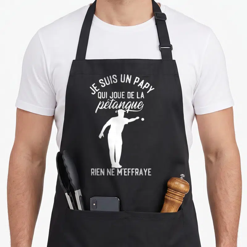 Tablier de cuisine noir avec une silhouette blanche d'un homme jouant à la pétanque et du texte humoristique en blanc.