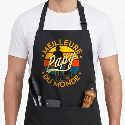 Tablier de cuisine noir avec motif vintage Meilleure Papy du Monde et silhouettes sur fond de soleil rayé orange et bleu.