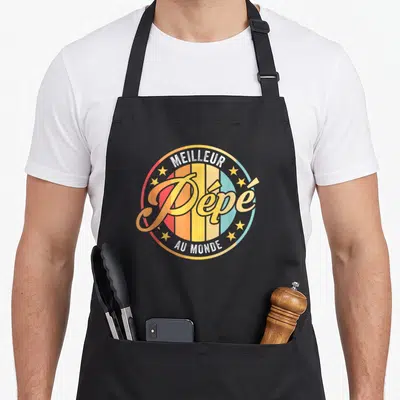 Tablier de cuisine noir avec logo circulaire rétro affichant Meilleur Pépé au monde en lettres dorées entouré d'étoiles.
