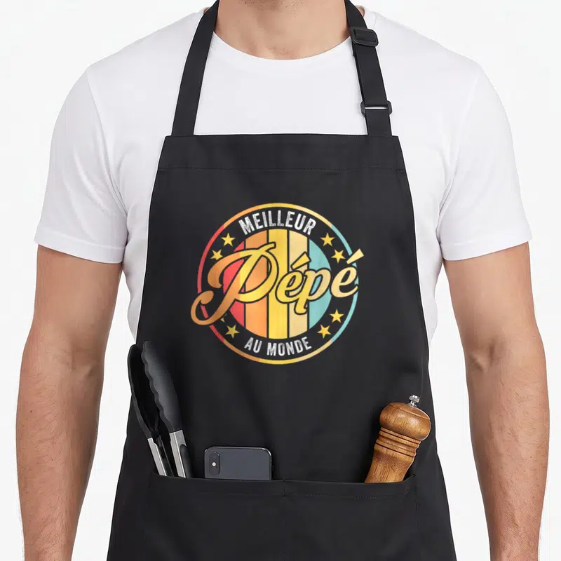 Tablier de cuisine noir avec logo circulaire rétro affichant Meilleur Pépé au monde en lettres dorées entouré d'étoiles.