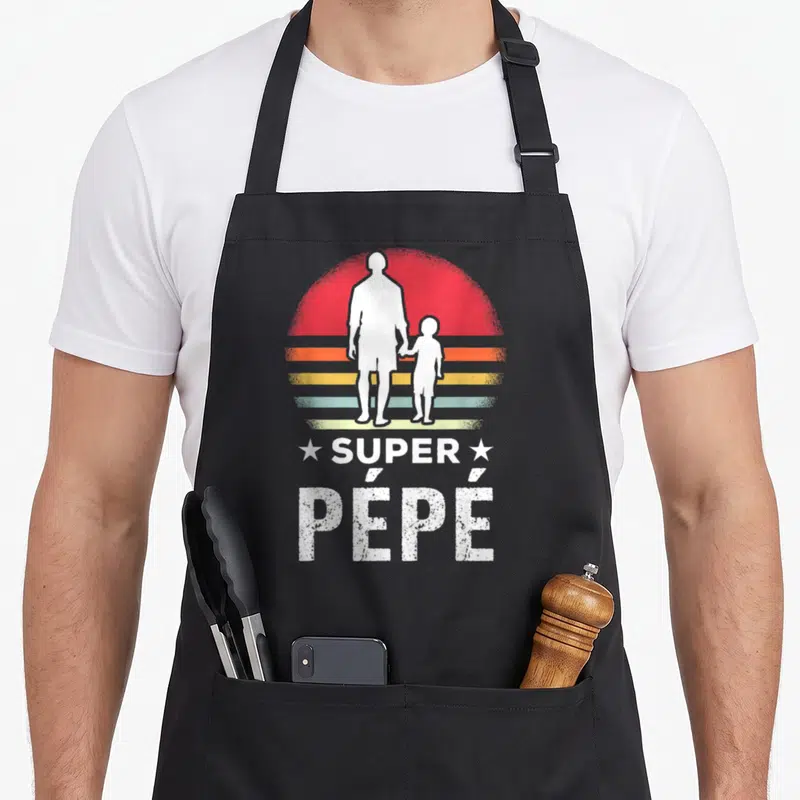 Tablier de cuisine noir avec silhouette blanc grand-père et enfant sur fond soleil rétro multicolore et texte Super Pépé en lettres capitales blanches usées.