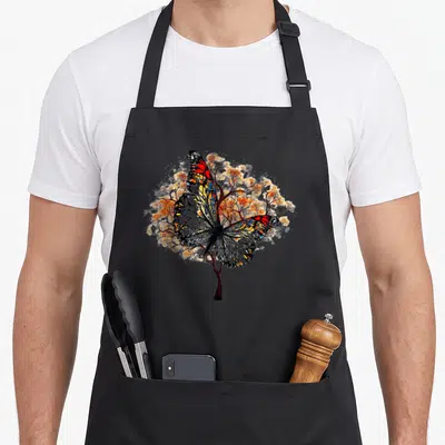 Tablier de cuisine noir avec un arbre papillon aux ailes orange, bleu et rouge se fondant dans les branches florales.