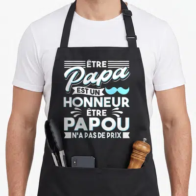 Tablier de cuisine noir avec inscription blanche et moustache bleue célébrant le rôle de papa et de grand-père.