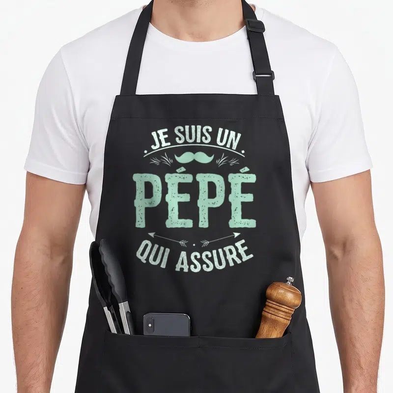 Tablier de cuisine noir avec inscription Je suis un Pépé qui assure et une moustache mint vert menthe au centre.