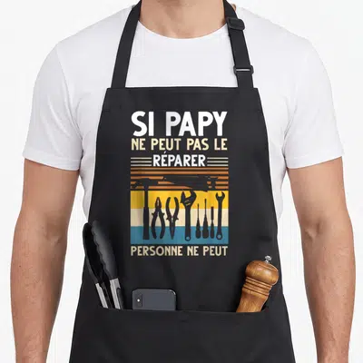 Tablier de cuisine noir avec inscription Si Papy ne peut pas le réparer et silhouettes d'outils vintage sur fond coloré.