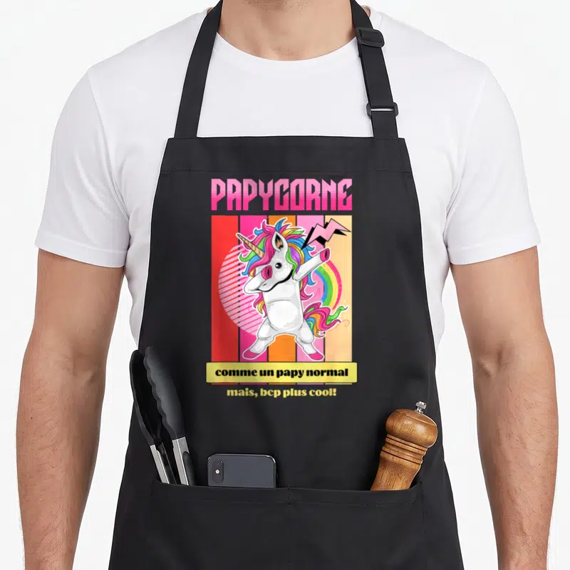 Tablier de cuisine noir avec une licorne blanche aux cheveux multicolores effectuant un mouvement de danse dab sur fond de rayures colorées et de foudre.