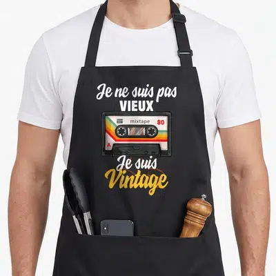 Tablier de cuisine noir avec illustration de cassette audio rétro et texte blanc jaune soulignant l'esprit vintage des années 80.