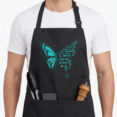 Tablier de cuisine noir avec un grand papillon turquoise et des textes inspirants sur le côté droit.