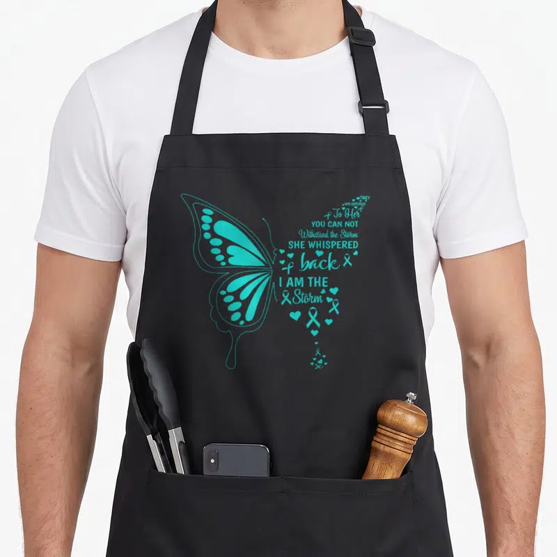 Tablier de cuisine noir avec un grand papillon turquoise et des textes inspirants sur le côté droit.