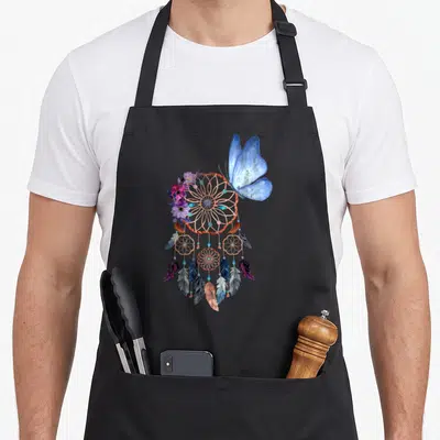 Tablier de cuisine noir avec attrape-rêves amérindien, papillon bleu et fleurs violettes imprimés au centre.