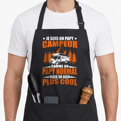 Tablier de cuisine noir avec inscription orange et blanc et illustration de camping-car entre des pins