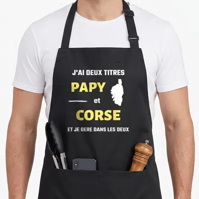 Tablier de cuisine noir avec texte blanc et jaune J'ai deux titres Papy et Corse et silhouette île.