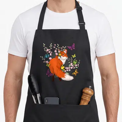 Tablier de cuisine noir avec un renard orange, des papillons multicolores et des fleurs roses.