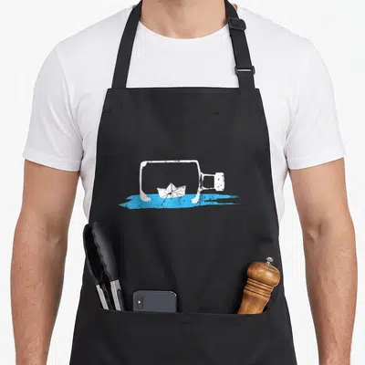 Tablier de cuisine noir avec un navire papier blanc dans une bouteille de courrier sur fond bleu.