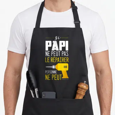 Tablier de cuisine noir avec texte blanc et jaune et illustration de perceuse électrique jaune au centre du motif imprimé.