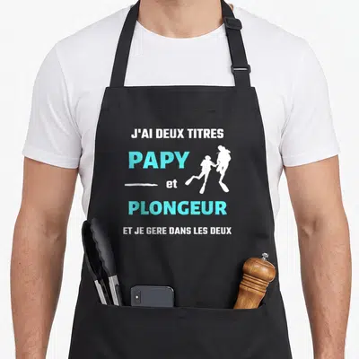 Tablier de cuisine noir avec texte J'ai deux titres Papy et Plongeur et silhouettes de plongeurs en bleu cyan.