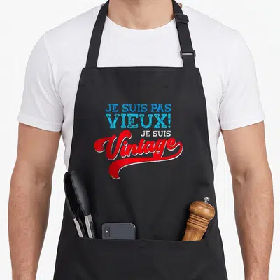 Tablier de cuisine noir avec l'inscription Je suis pas vieux je suis vintage en bleu et rouge.