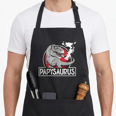 Tablier de cuisine noir avec illustration d'un dinosaure fumant et du texte Papysaurus en blanc sur fond rouge.