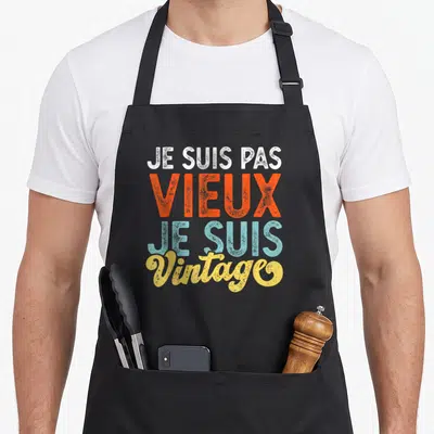 Tablier de cuisine noir avec le texte coloré Je suis pas vieux je suis vintage imprimé au centre du torse.