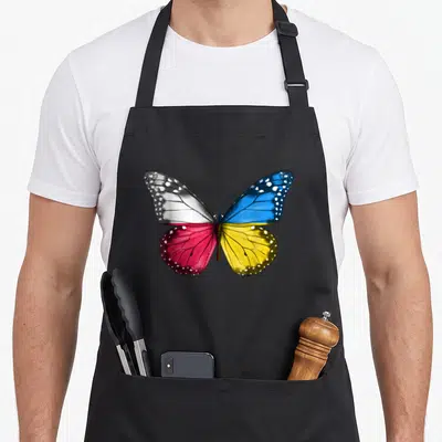 Tablier de cuisine noir avec un grand papillon aux ailes aux couleurs du drapeau polonais et ukrainien.