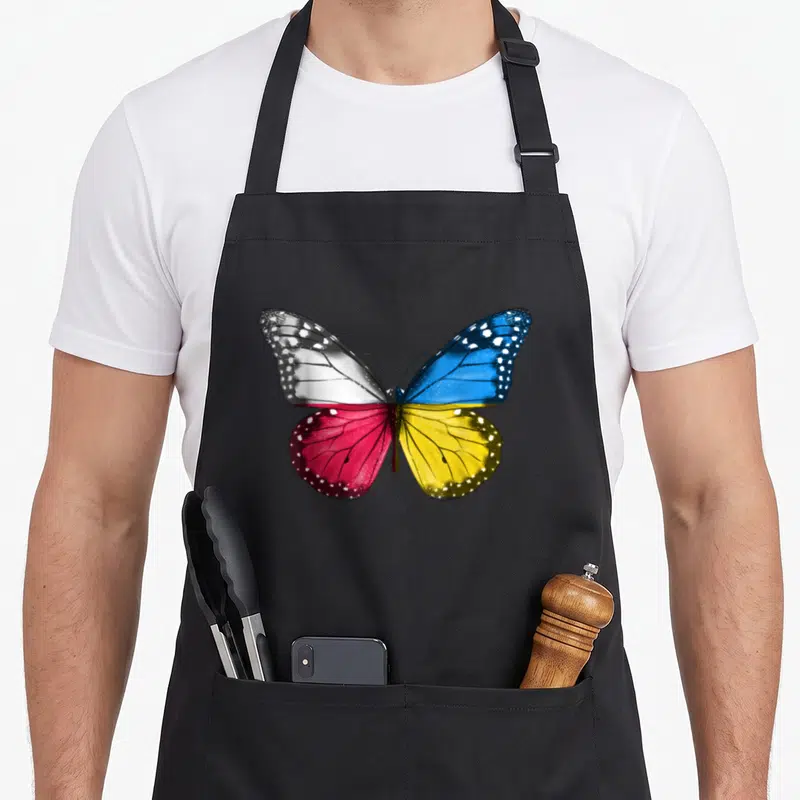 Tablier de cuisine noir avec un grand papillon aux ailes aux couleurs du drapeau polonais et ukrainien.