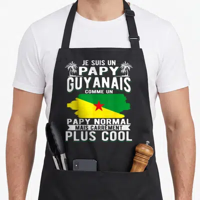 Tablier de cuisine noir avec texte blanc et drapeau vert jaune rouge stylisé entouré de palmiers.