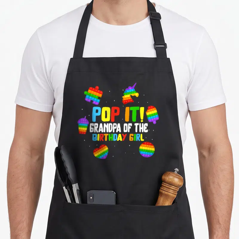 Tablier de cuisine noir avec des pop it colorés et le texte Pop It Grandpa of the anniversaire Girl imprimé au centre.