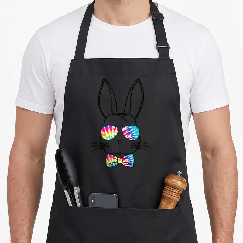 Tablier de cuisine noir avec tête de lapin portant des lunettes tie-dye et un nœud papillon multicolore.