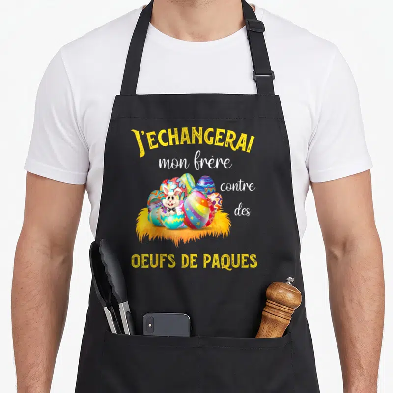 Tablier de cuisine noir avec un lapin en nœud papillon entouré d'œufs de Pâques colorés et une phrase humoristique jaune et blanche.