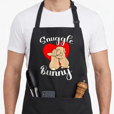 Tablier de cuisine noir avec deux lapins marron s'embrassant devant un grand cœur rouge et les mots Snuggle Bunny en blanc.