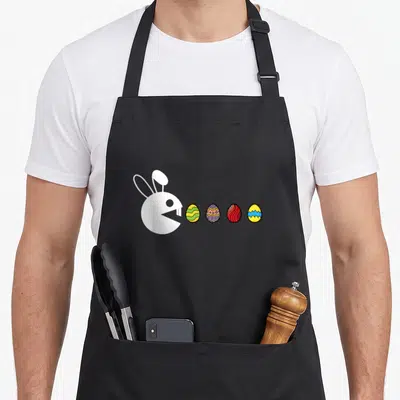 Tablier de cuisine noir avec illustration blanche d'un lapin type Pac-Man face à quatre œufs de Pâques décorés.