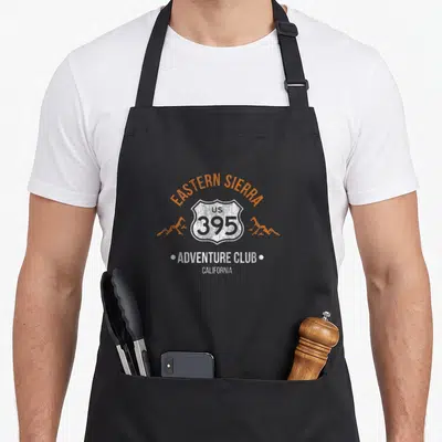 Tablier de cuisine noir avec l'inscription Eastern Sierra US 395 Adventure Club en orange et blanc.