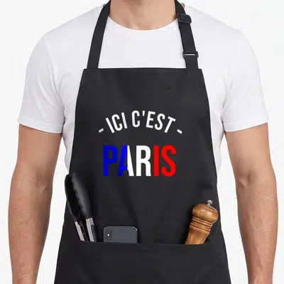 Tablier de cuisine noir avec inscription Ici c'est Paris en lettres bleues blanches et rouges.