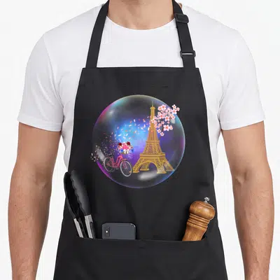Tablier de cuisine noir avec une illustration de bulle contenant la Tour Eiffel, un vélo rose et des fleurs colorées.